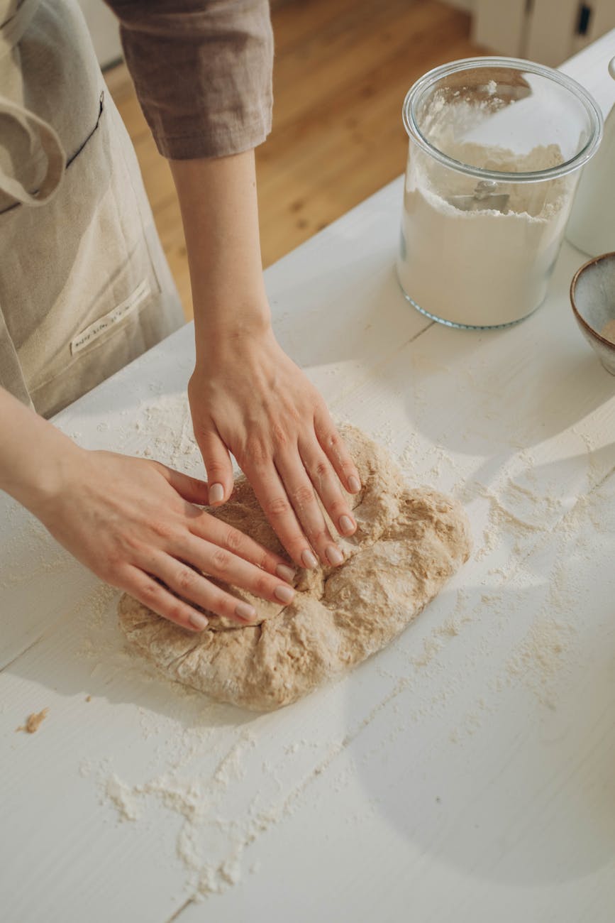a person kneading a dough on the white surface