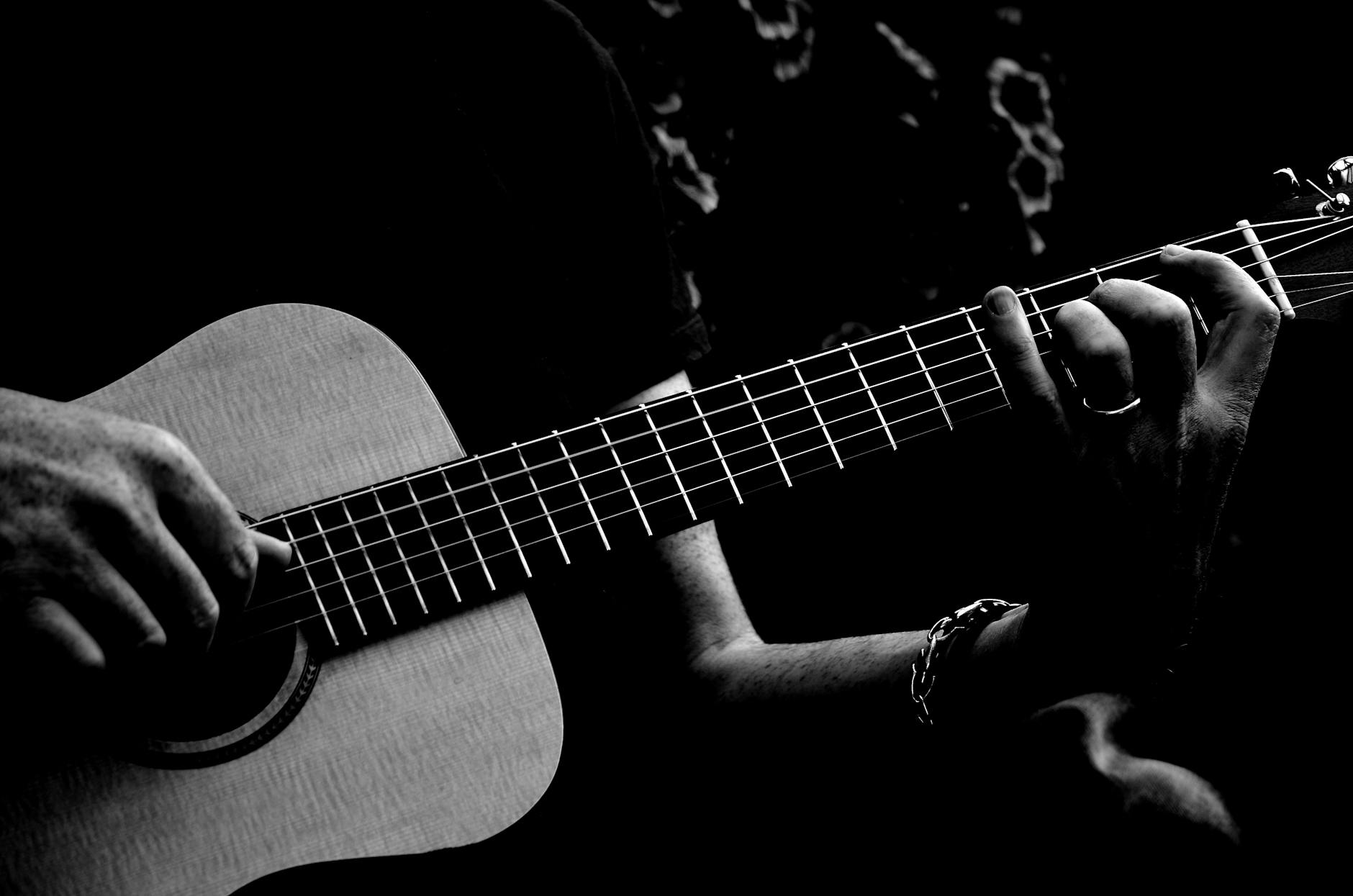 monochrome photo of person playing acoustic guitar